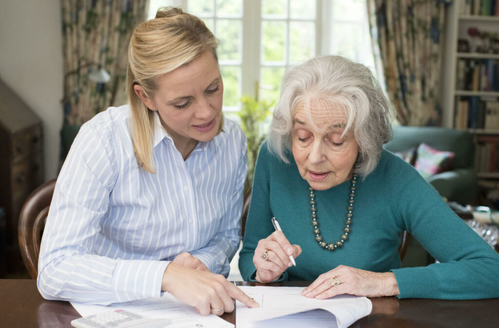 A young woman sitting at a table with a senior woman helping her with paperwork.