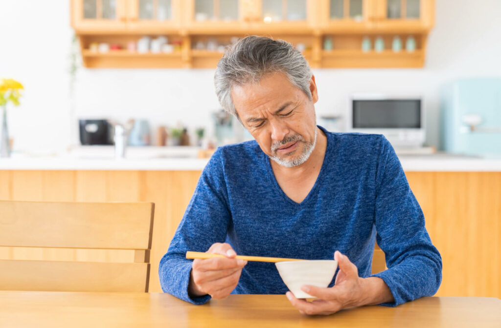 A senior man in a blue v-neck shirt looking at his unappetizing meal.