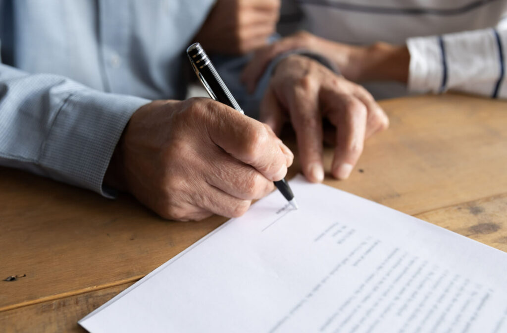 A close-up of an older adult man signing a power of attorney document.
